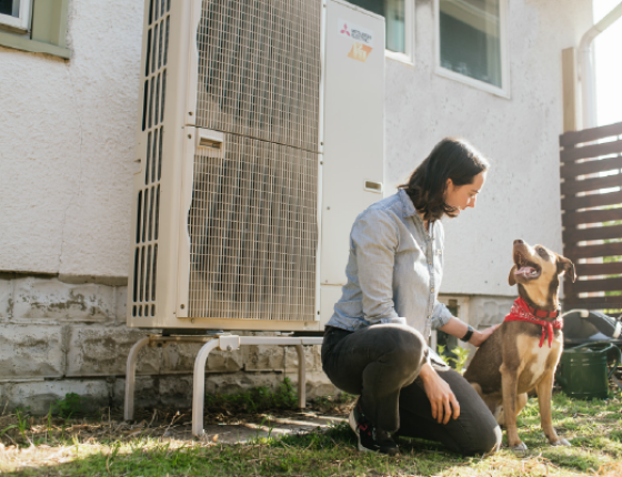 homeowner kneeling next to outdoor heat pump unit with dog