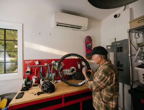 Man working on bike wheel in workshop below a mini-split unit on the wall