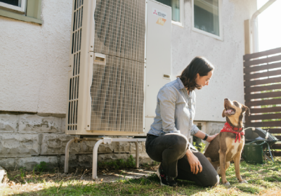 homeowner kneeling next to outdoor heat pump unit with dog