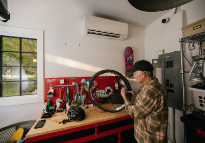 Man working on bike wheel in workshop below a mini-split unit on the wall