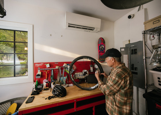 Man working on bike wheel in workshop below a mini-split unit on the wall