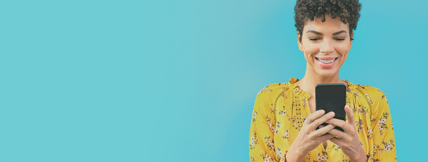 A woman in a yellow shirt looks at her phone.