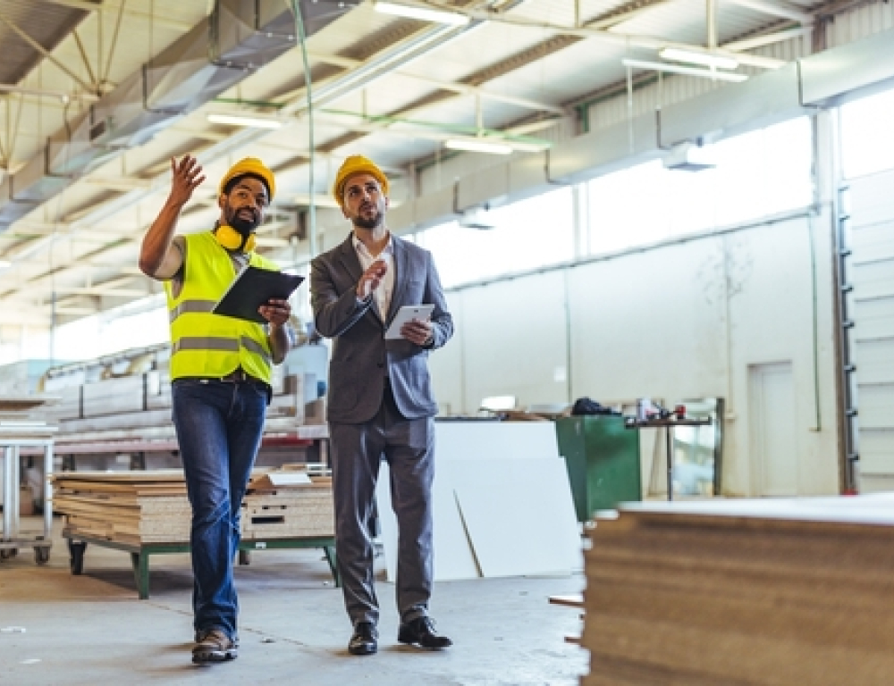 Two people stand side by side in hard hats. One is in jeans and a hi-vis vest and the other is in a suit.