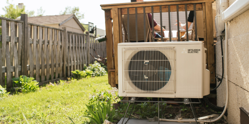 A heat pump next to a deck in a backyard.