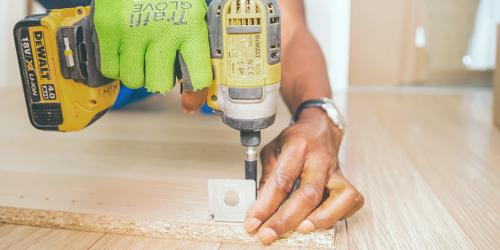 Hands wearing a glove use a drill on a floor.
