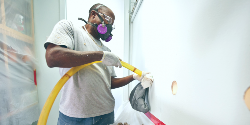 A man wearing PPE works on a wall.