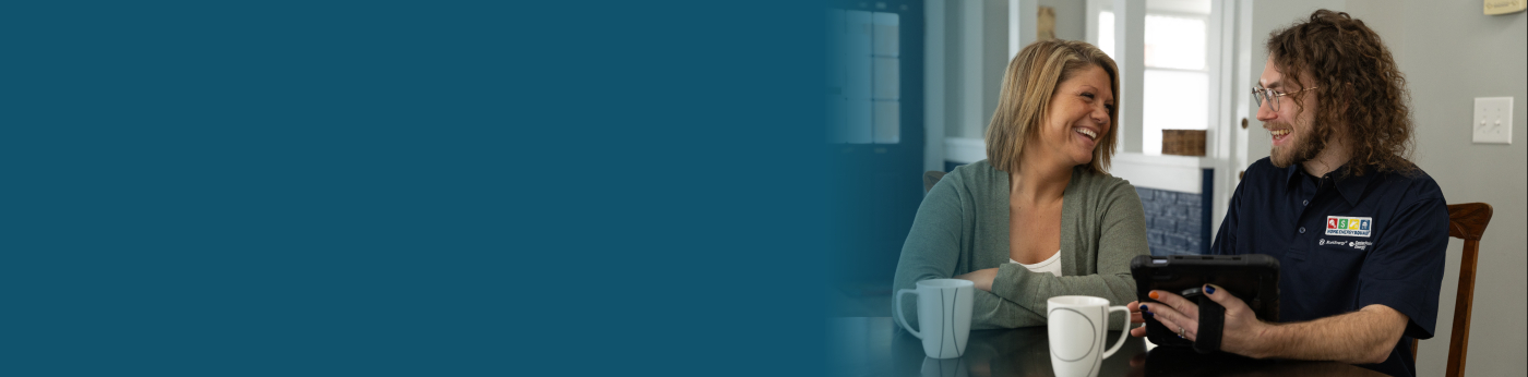 A homeowner and auditor sit in the home reviewing the home's audit findings on an iPad.