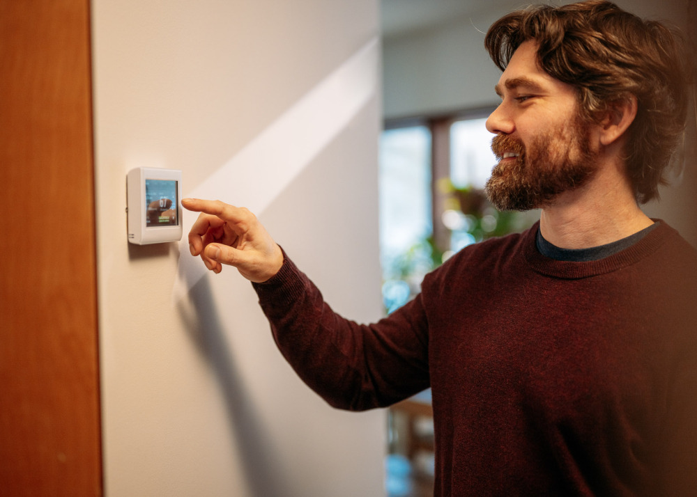 A man in a sweater adjusts the thermostat in his home.