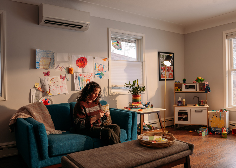 A woman sits on a couch knitting in her home.
